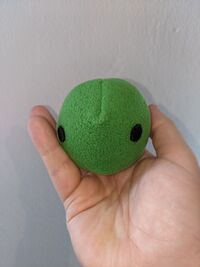 A green plush "poison" physrep, about 5cm wide, held in a hand.
